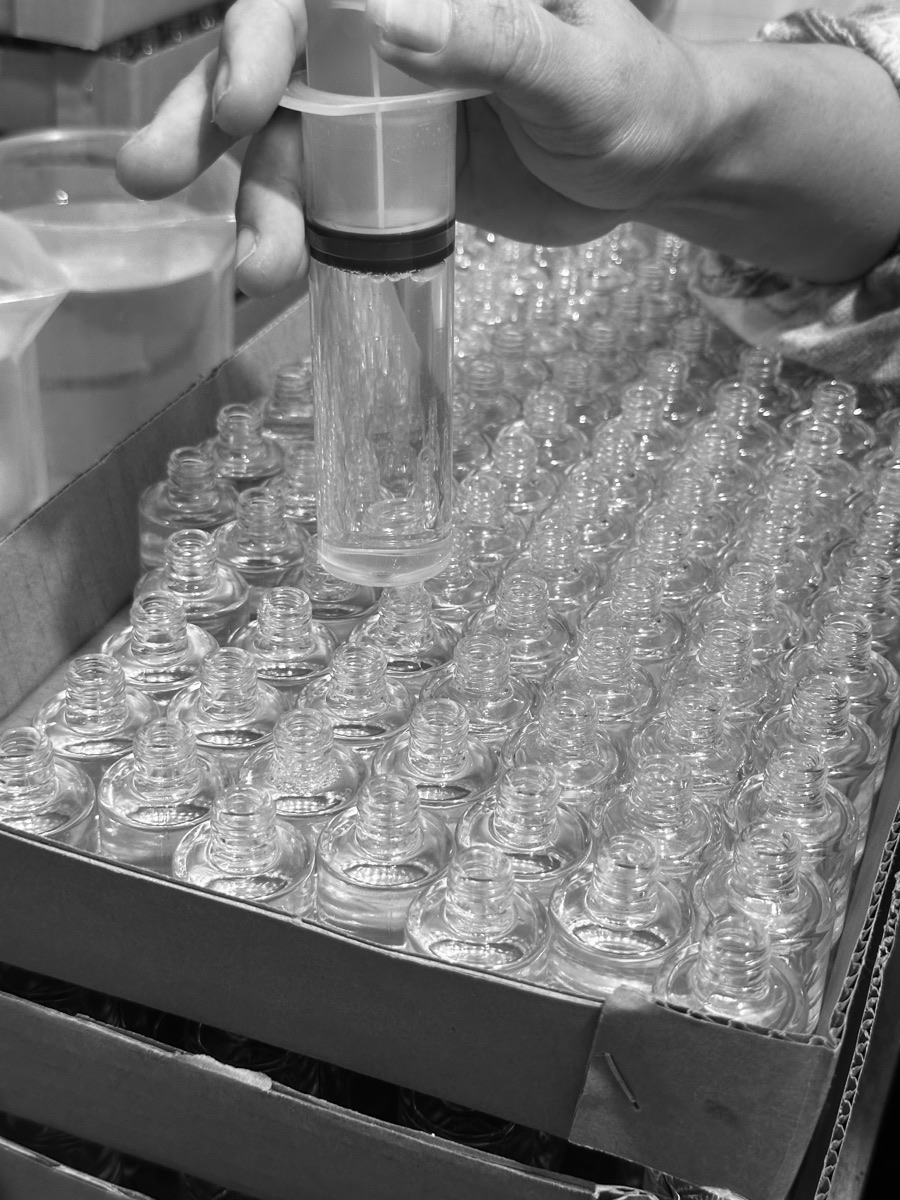 Botol-botol kaca ORMOY sedang diisi di lini produksi, foto hitam putih.
